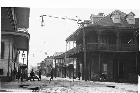 A French Quarter street corner in New Orleans around 1880, with iron galleries and a gas lamp.