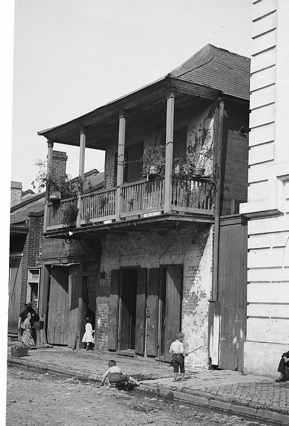 An old two-story house with a wooden gallery on a French Quarter street, New Orleans, around 1880.